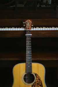 An acoustic guitar resting against a piano