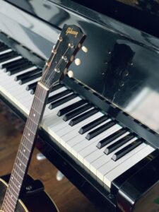 A black guitar resting on a Grand Piano