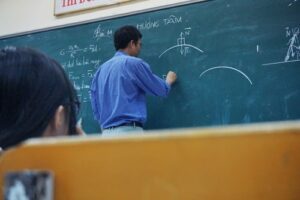 A teacher in a classroom writing on a blackboard in chalk