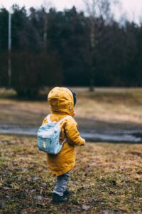 A child in a yellow coat walking in the woods with a backpack